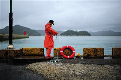 7月6日，韓國(guó)珍島，一名海岸警察在港口系救生圈。4月，客輪在珍島近海發(fā)生沉船事故后，仍有11人下落不明。